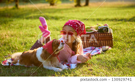 Girl in red bandana lying on blanket with dog in sunglasses enjoying picnic Girl in red bandana lying on blanket with dog in sunglasses enjoying picnic 130929741