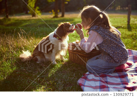 Girl offering peach to dog at picnic with sunlight on grass Girl offering peach to dog at picnic with sunlight on grass 130929771