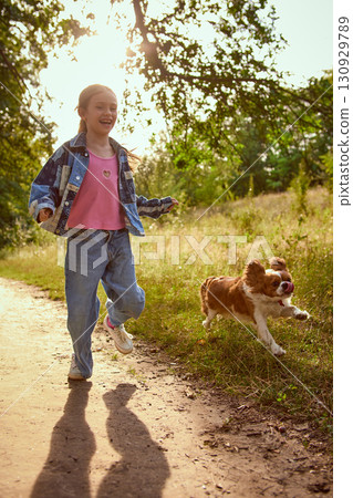 Girl laughing while running with dog in meadow under sunlight 130929789