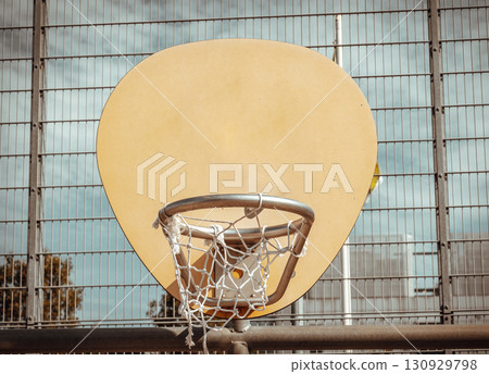 an oval-shaped wooden backboard, a metal hoop ring and a white net, all positioned against a wire fence in the background at outdoor basketball courts 130929798