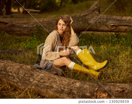 Woman in yellow boots resting on log with thoughtful gaze in autumn forest Woman in yellow boots resting on log with thoughtful gaze in autumn forest 130929839