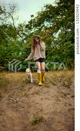 Woman walking with dog in yellow boots on forest trail 130929942