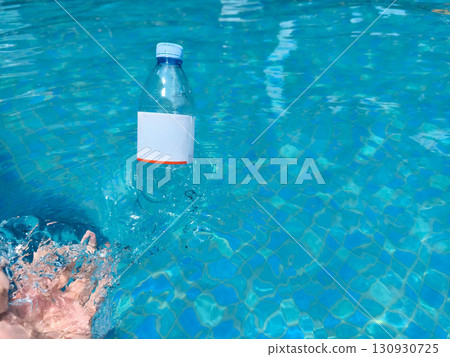 A hand lifts a plastic bottle from clear blue pool water, symbolizing pollution cleanup and environmental awareness. A hand lifts a plastic bottle from clear blue pool water, symbolizing pollution cleanup and environmental awareness. 130930725