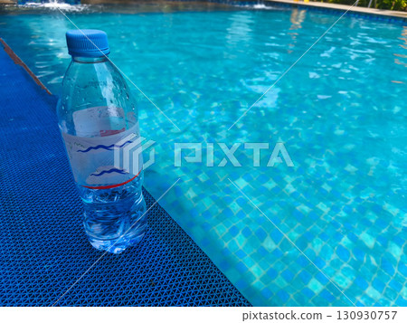 Plastic water bottle placed on the edge of a swimming pool, symbolizing refreshment and hydration during summer activities. Plastic water bottle placed on the edge of a swimming pool, symbolizing refreshment and hydration during summer activities. 130930757