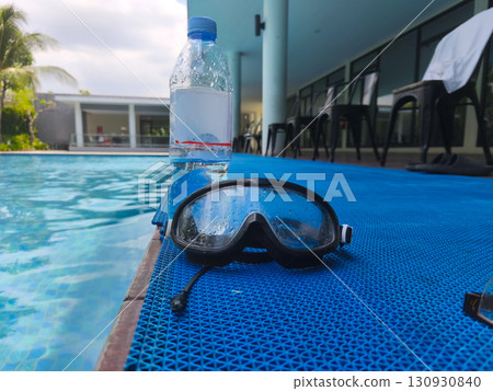 Plastic water bottle and wet swimming goggles on poolside mat, symbolizing summer recreation, hydration, and swimming activities. Plastic water bottle and wet swimming goggles on poolside mat, symbolizing summer recreation, hydration, and swimming activities. 130930840