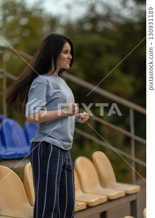 brunette girl stands alone in an empty stadium dressed in a blue t shirt. With her hair flowing she shows excitement and joy celebrating a hard earned victory in the fresh air. 130931189