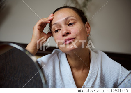 Thoughtful Woman in White Bathrobe Reflecting in Front of a Mirror Thoughtful Woman in White Bathrobe Reflecting in Front of a Mirror 130931355