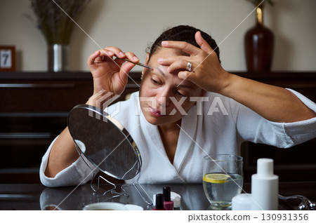 Woman Grooming Eyebrows with Tweezer in Bathroom Vanity Routine Woman Grooming Eyebrows with Tweezer in Bathroom Vanity Routine 130931356