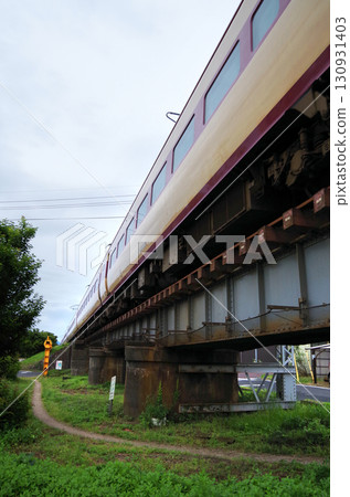 A 381 series Yakumo express train, painted in the old JNR colors as part of a revival project, passes through a low-profile iron bridge in the city. 130931403