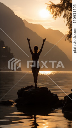 Silhouette of a woman doing yoga, standing on a rock by the water at sunset, arms raised in a peaceful pose Silhouette of a woman doing yoga, standing on a rock by the water at sunset, arms raised in a peaceful pose 130931503