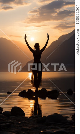 Silhouette of a woman on a rocky shore during sunset, with arms up, with the sun reflecting on the water 130931504