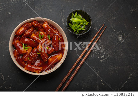 Traditional Korean tteokbokki served on white plate with chopsticks and sesame seeds on black rustic background, space for text 130932212