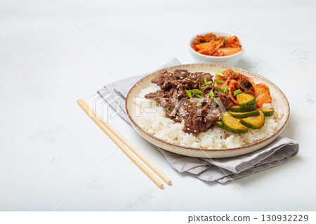 Korean beef bulgogi bowl dish with rice, roasted meat, kimchi and marinated cucumber on white background with chopsticks, space for text 130932229