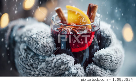 Warm mulled wine with an orange slice and a cinnamon stick in a glass, a winter drink in snow-white woolen mittens Warm mulled wine with an orange slice and a cinnamon stick in a glass, a winter drink in snow-white woolen mittens 130933834