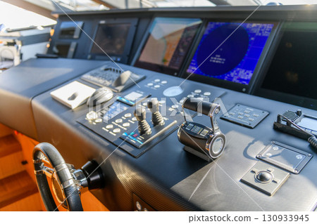 A close-up view of a yacht or ship bridge with the throttle controls. The navigation radar screen and electronic control panels are visible in the background, emphasizing modern marine technology and A close-up view of a yacht or ship bridge with the throttle controls. The navigation radar screen and electronic control panels are visible in the background, emphasizing modern marine technology and 130933945