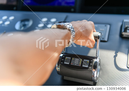 A close up view of a yacht or ship bridge with a captains hand operating the throttle controls. 130934006