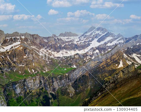 Breathtaking view of snow-capped mountains and lush valleys under a bright blue sky 130934405