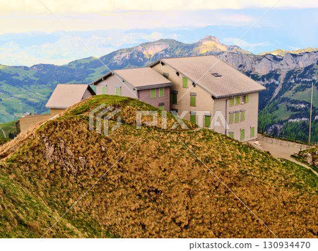 Mountain lodge rests atop a grassy hill with panoramic views of the surrounding landscape during sunset 130934470