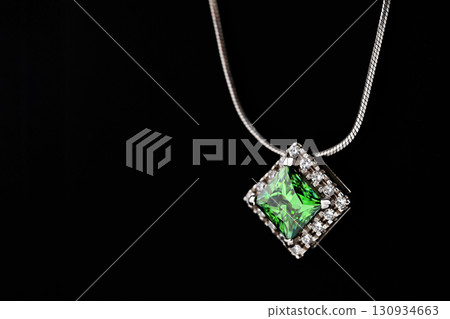 A green gemstone pendant is displayed on a black background A green gemstone pendant is displayed on a black background 130934663