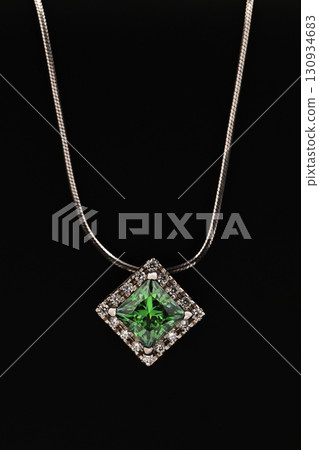 A green gemstone pendant is displayed on a black background A green gemstone pendant is displayed on a black background 130934683