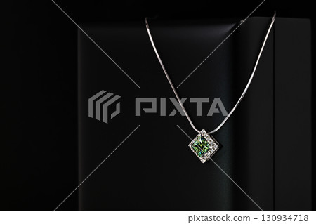 A green gemstone pendant is displayed on a black background A green gemstone pendant is displayed on a black background 130934718