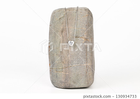 A silver necklace with a heart shaped pendant is displayed on a gray stone 130934733