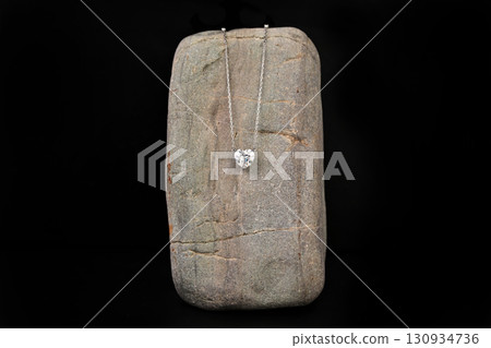 A silver necklace with a heart pendant sits on a rock A silver necklace with a heart pendant sits on a rock 130934736