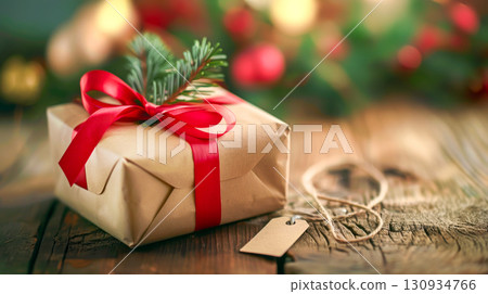 Rustic Christmas gift, wrapped in brown paper with red ribbon and pine branch, rests on wooden table, evoking cozy holiday atmosphere. Concept of eco-friendly wrapping and handmade holiday traditions 130934766