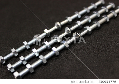 Shiny Iron Bolts With Nuts Screwed On Them Lie In Even Rows Isolated On Black Surface 130934776