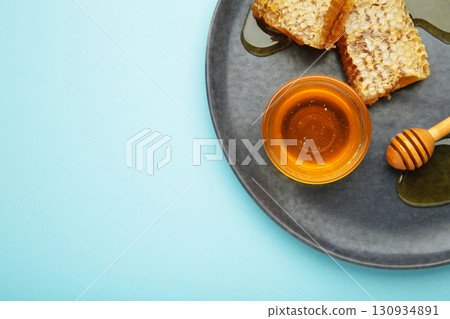 Bowl of sweet honey, dippers and combs on dark plate on blue background Bowl of sweet honey, dippers and combs on dark plate on blue background 130934891