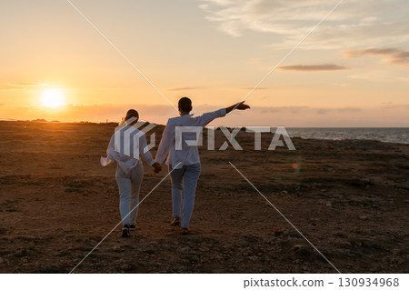 Couple Sunset Beach Walking - Silhouette of a couple walking hand in hand on the beach at sunset. Couple Sunset Beach Walking - Silhouette of a couple walking hand in hand on the beach at sunset. 130934968