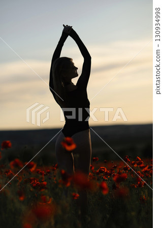 Silhouette Woman Poppies: Sunset silhouette girl stretches in poppy field for relaxation, evening golden hour. Silhouette Woman Poppies: Sunset silhouette girl stretches in poppy field for relaxation, evening golden hour. 130934998