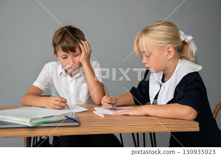 Children School Homework Study - Two children in school uniforms sitting at a desk doing homework. Children School Homework Study - Two children in school uniforms sitting at a desk doing homework. 130935023