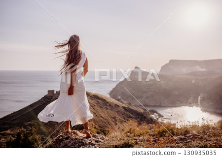 A woman in a white dress stands on a hill overlooking the ocean. The scene is serene and peaceful, with the woman's dress billowing in the wind. The combination of the ocean. A woman in a white dress stands on a hill overlooking the ocean. The scene is serene and peaceful, with the woman's dress billowing in the wind. The combination of the ocean. 130935035