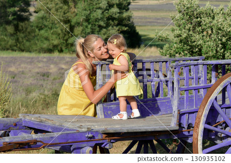 Mother and daughter in yellow dresses near a Wooden horse cart in a field of lavender Mother and daughter in yellow dresses near a Wooden horse cart in a field of lavender 130935102