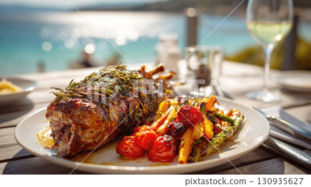 A gourmet dish featuring perfectly cooked rack of lamb with side of roasted asparagus, carrots, and tomatoes. Meal is served on white plate on a wooden table, with the sparkling blue sea background A gourmet dish featuring perfectly cooked rack of lamb with side of roasted asparagus, carrots, and tomatoes. Meal is served on white plate on a wooden table, with the sparkling blue sea background 130935627
