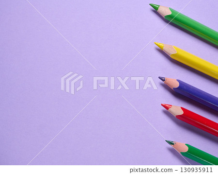 A row of sharpened colored pencils arranged diagonally on a blue background, close-up 130935911