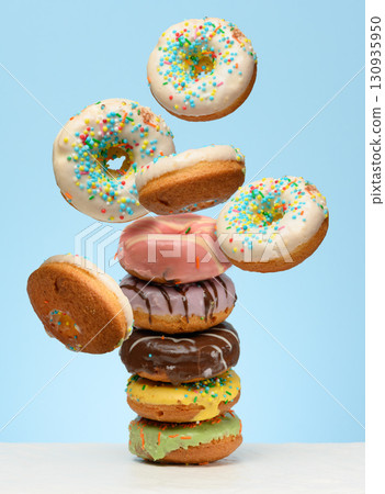 A stack  glazed donuts on a table. White donuts with sprinkles flying around them 130935950