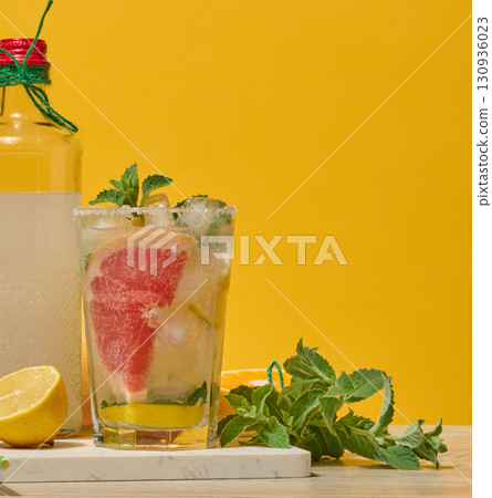 A glass with a drink and a bottle of lemonade on a rich yellow background. Lemon, mint and grapefruit are on the table A glass with a drink and a bottle of lemonade on a rich yellow background. Lemon, mint and grapefruit are on the table 130936023