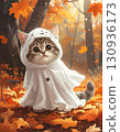 A cat with a small ghost costume is sitting on a pile of autumn leaves. 130936173