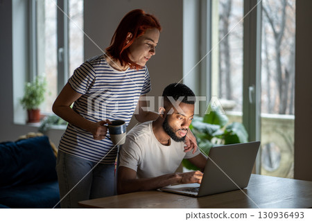 Loving woman wife standing behind husband working on laptop, supporting him in online business Loving woman wife standing behind husband working on laptop, supporting him in online business 130936493