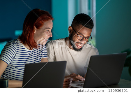 Happy diverse couple have small online business at home work on laptops in evening 130936501