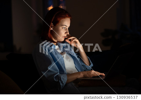 Focused freelancer woman looking laptop screen at night working from home.  130936537