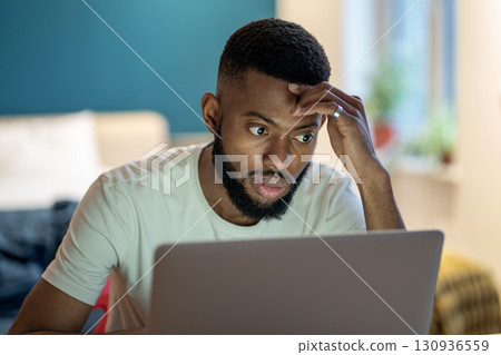 Focused African American guy freelancer working on laptop at home office, feeling overwhelmed 130936559