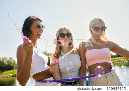 Three friends enjoying a sunny day outdoors with bubbles and smiles 130937115