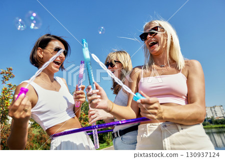 Group of Women Having Fun Blowing Bubbles on a Sunny Day Outdoors 130937124