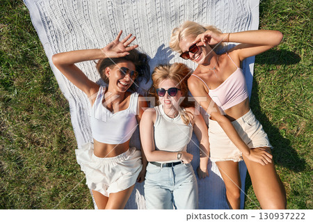 Three friends relaxing on a picnic blanket outdoors in sunshine 130937222