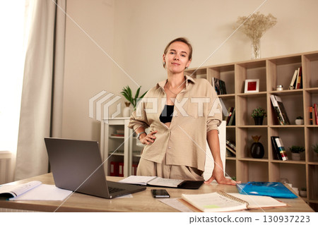 Confident professional woman standing in her office space surrounded by work materials Confident professional woman standing in her office space surrounded by work materials 130937223