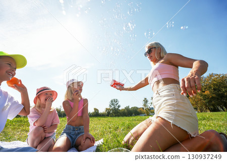 Family enjoying a sunny picnic with bubbles in a green park 130937249