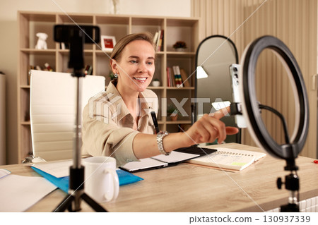 Woman recording a video in home office with ring light and smartphone Woman recording a video in home office with ring light and smartphone 130937339